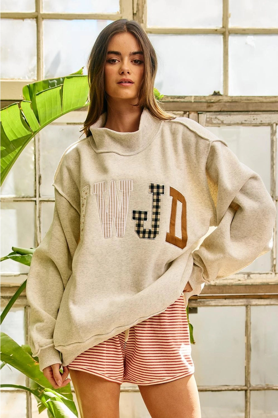 Woman wearing a beige sweatshirt with text and pink shorts in a room with plants.