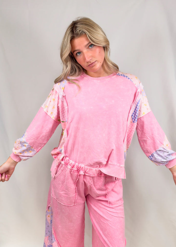 Woman wearing pink top and bottoms with patchwork detail on plain background