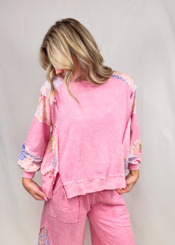 Woman wearing pink top and bottom with patchwork detail on plain background