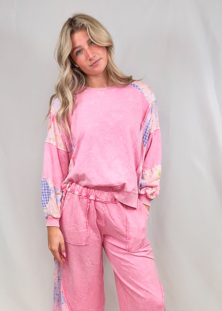 Woman wearing matching pink top and bottom with patchwork detail on plain background