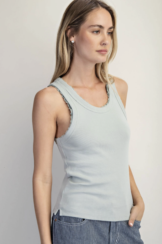 Woman wearing a light blue tank top with lace trim on a plain background