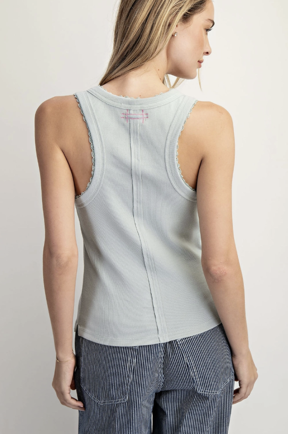Woman wearing a light gray tank top and dark pants against a plain background