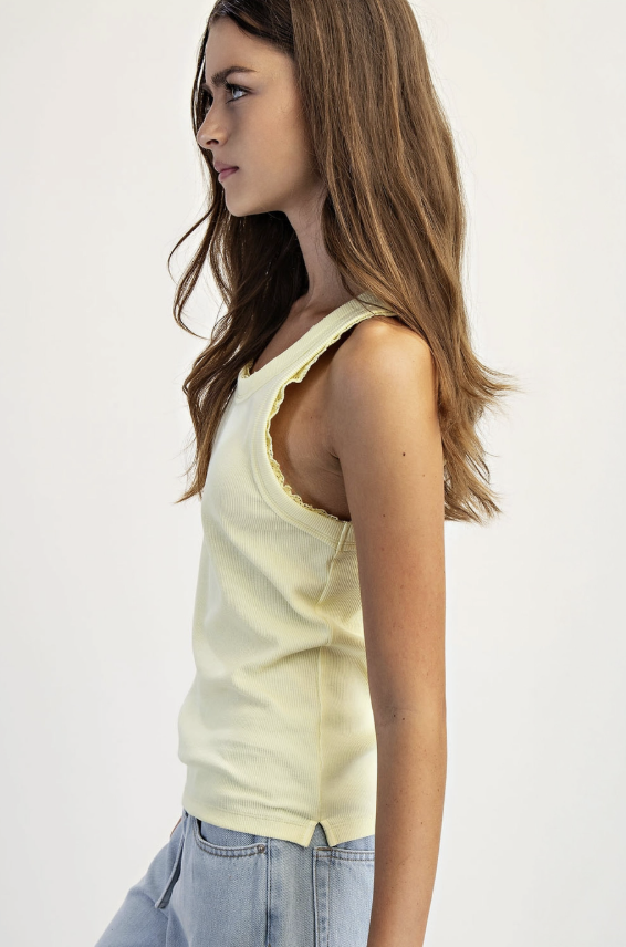 Woman wearing a light yellow tank top with ruffled trim on a plain background