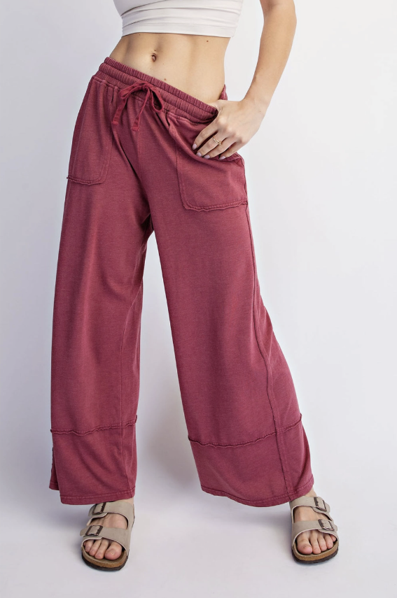 A person wearing wide-leg drawstring pants in a dusty rose or mauve shade, paired with beige slide sandals, shown from the waist down against a light gray studio background.