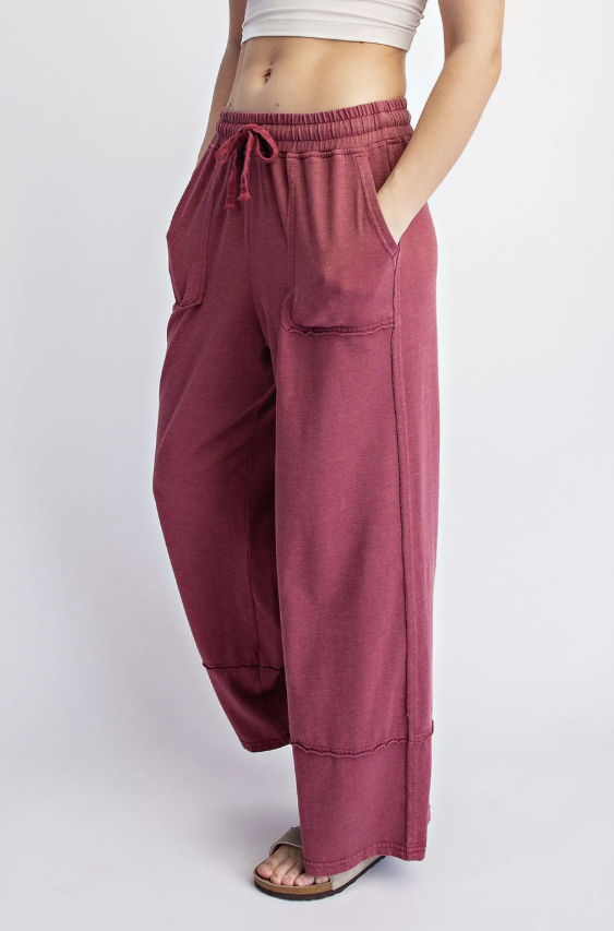 A person wearing loose, wide-leg dusty rose pants with an elastic drawstring waist, side pockets, and cuffed hems, shown against a light gray studio background.