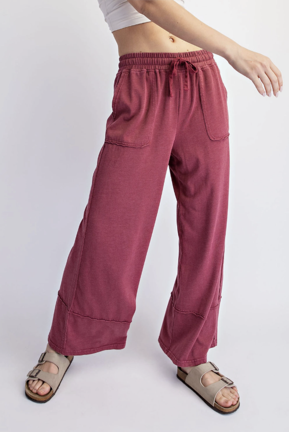 A person wearing loose, wide-leg drawstring pants in a dusty rose or mauve shade, paired with beige double-strap sandals, shown against a plain light gray studio background.