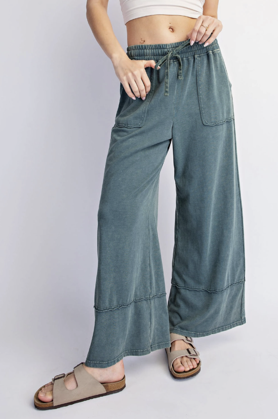 A person wearing wide-leg, cropped wide-leg pants in a muted blue-gray color, styled with beige slide sandals against a light gray studio background.