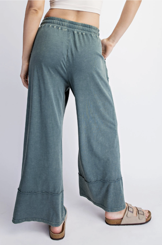 A person wearing wide-leg cropped pants in a washed slate blue-green color, shown from the back against a light gray studio background.