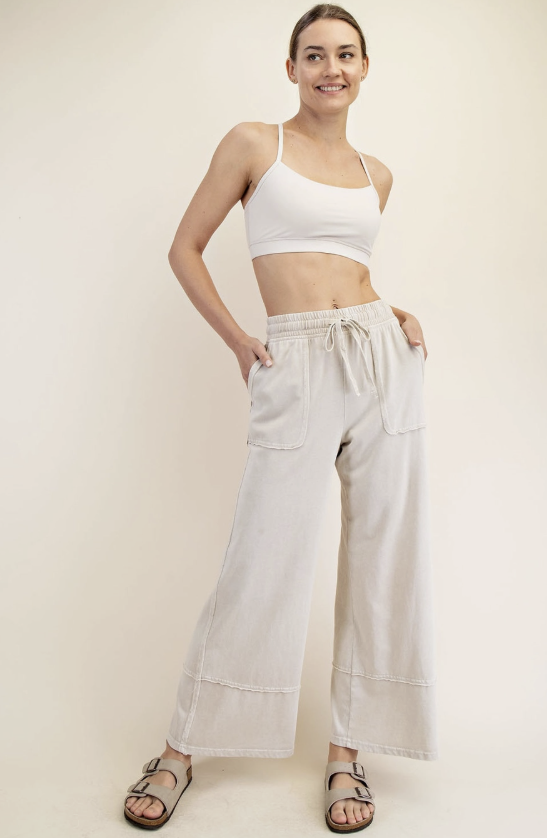 Woman wearing a white crop top and light-colored wide-leg pants on a plain background