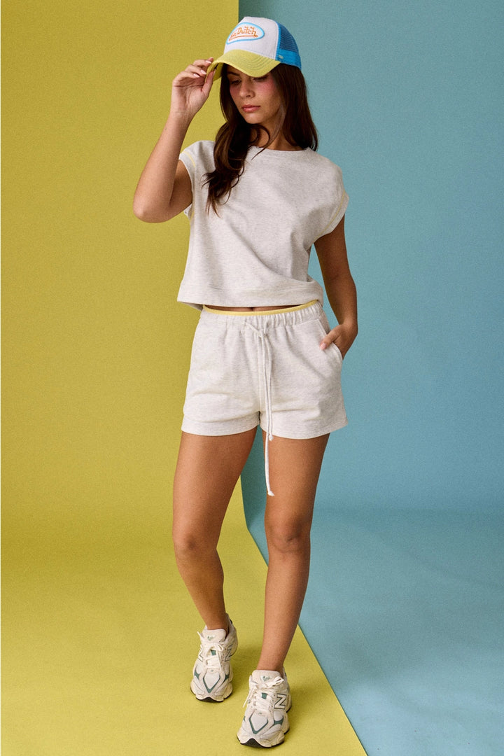 Woman wearing a white t-shirt, beige shorts, and a colorful cap on a two-tone yellow and blue background