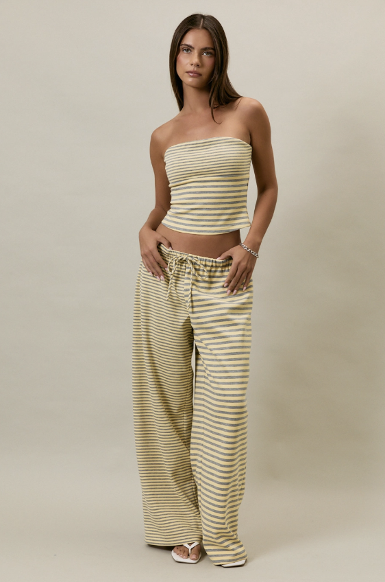 A woman modeling a matching two-piece set consisting of a strapless cropped top and wide-leg drawstring pants, both in a beige and olive green striped pattern, set against a plain beige studio background.