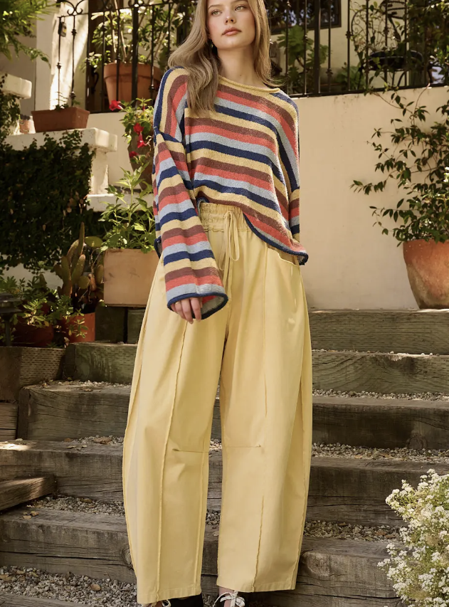 A woman stands on outdoor wooden steps wearing a multicolor striped knit sweater and high-waisted, wide-leg yellow pants.
