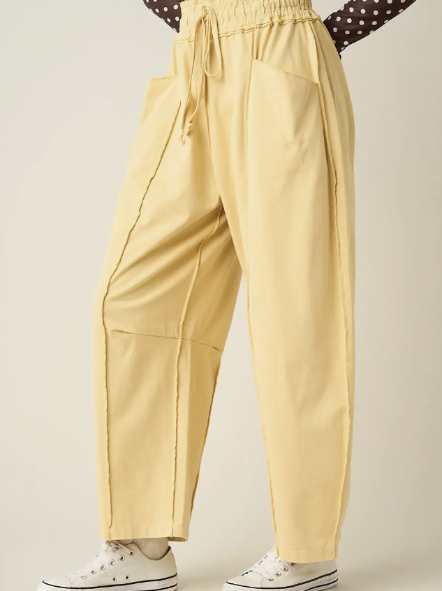 A person wearing loose, wide-leg yellow drawstring pants with large front patch pockets, shown from the waist down against a plain light beige studio background. White sneakers are also visible.