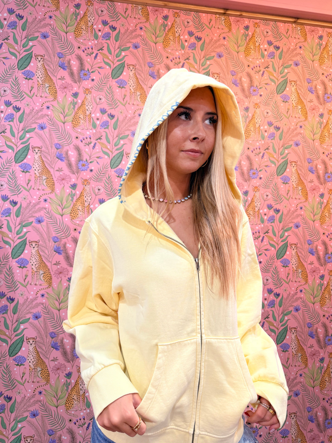Close up of stitching detail on yellow hoodie on pink floral background