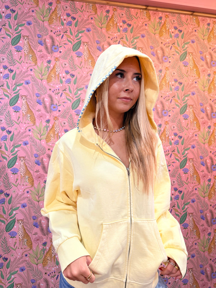 Close up of stitching detail on yellow hoodie on pink floral background