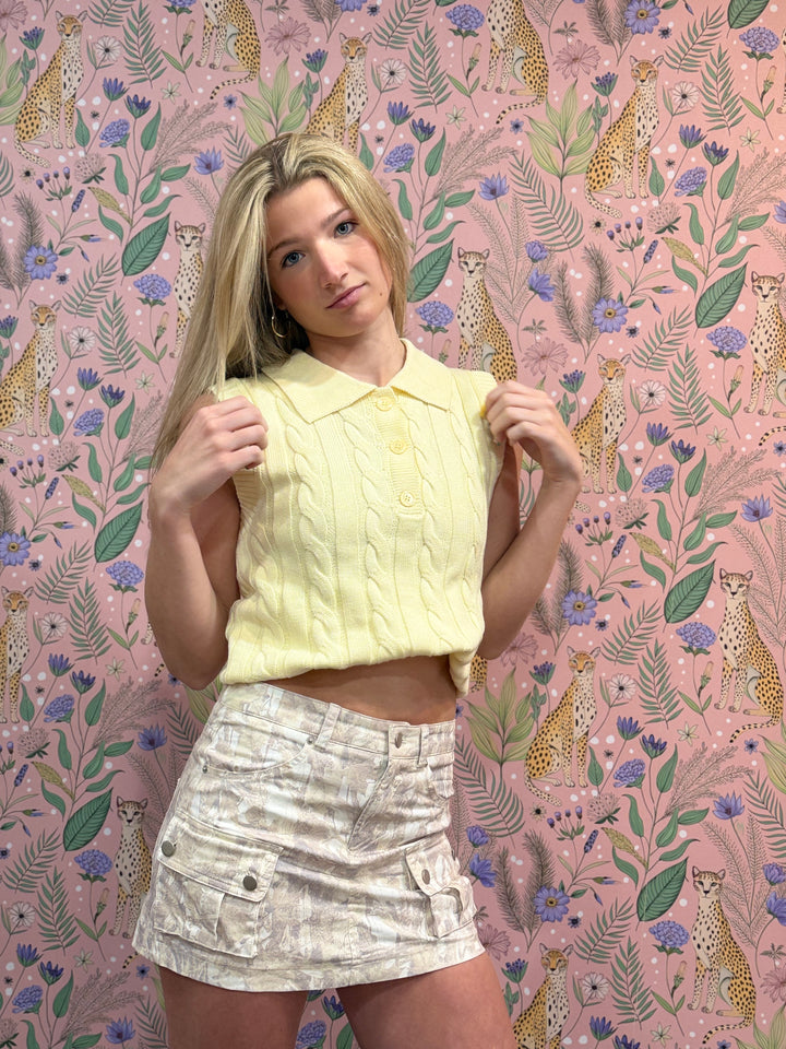 Woman wearing a yellow top and white skirt against a pink floral and animal patterned background