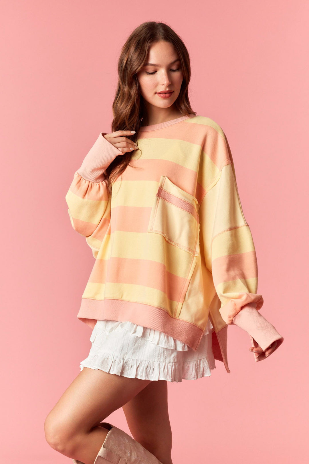 Woman wearing a colorful striped sweater and white shorts on a pink background