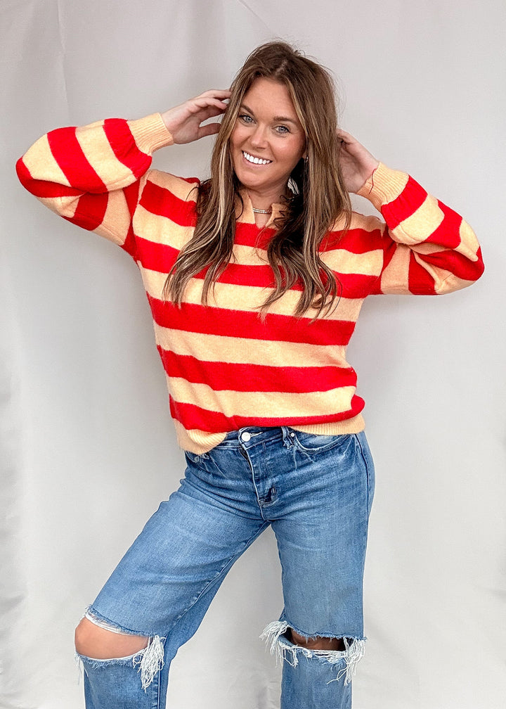 Woman wearing red and salmon stripe sweater with jeans on plain background