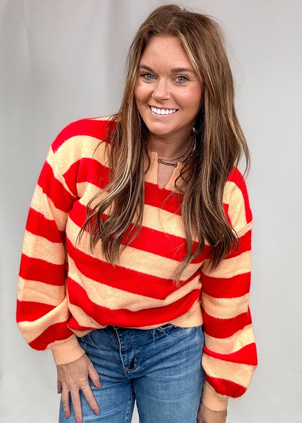 Woman wearing red and salmon stripe sweater with jeans on plain background