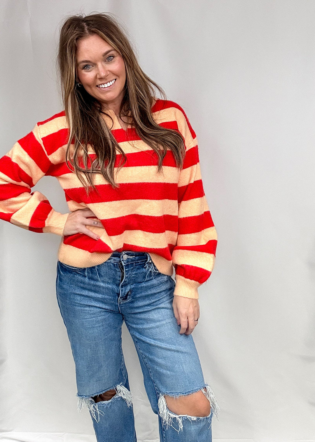 Woman wearing red and salmon stripe sweater and jeans on plain background