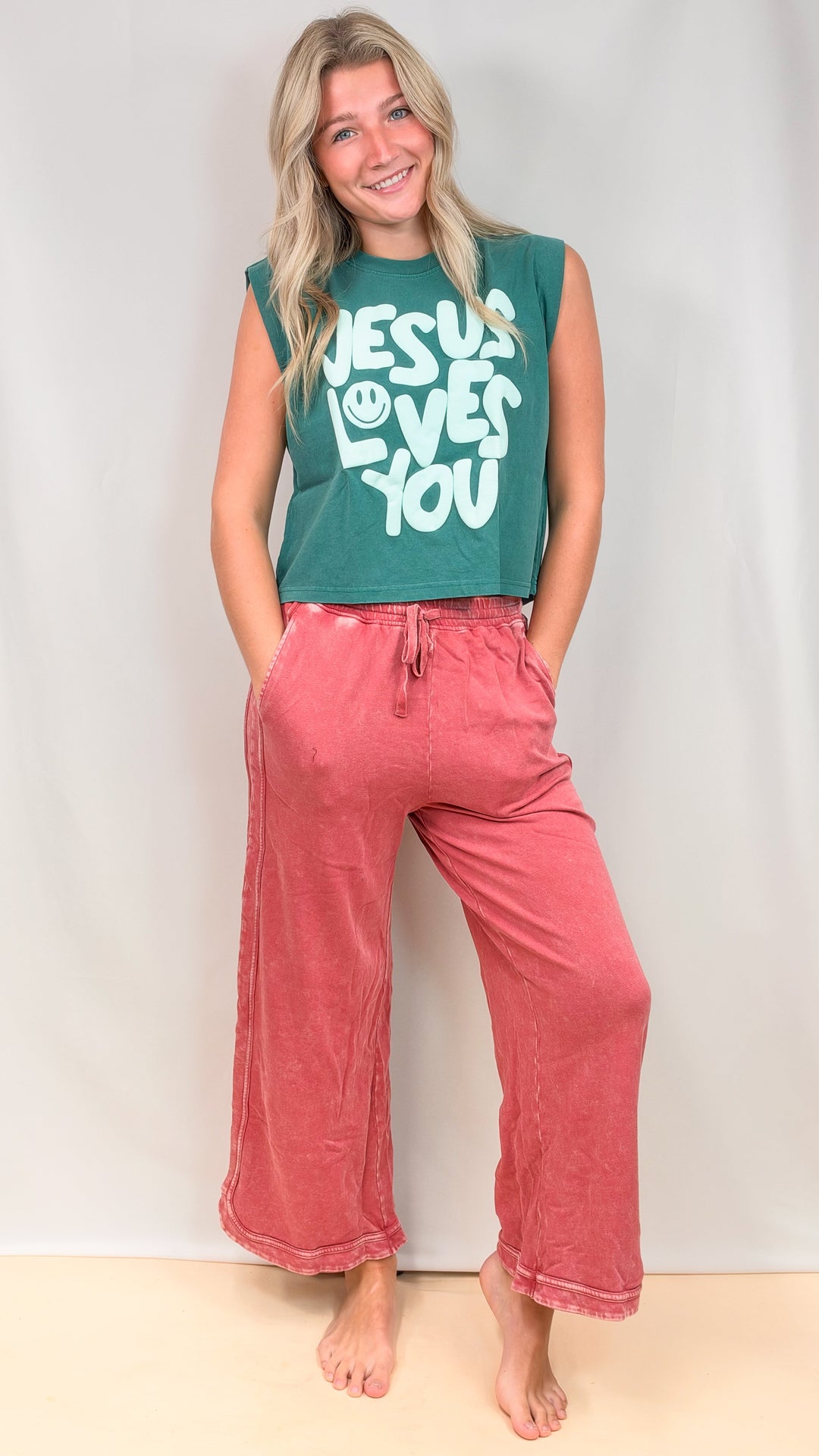 Woman wearing teal muscle tee and raspberry color pants on plain background