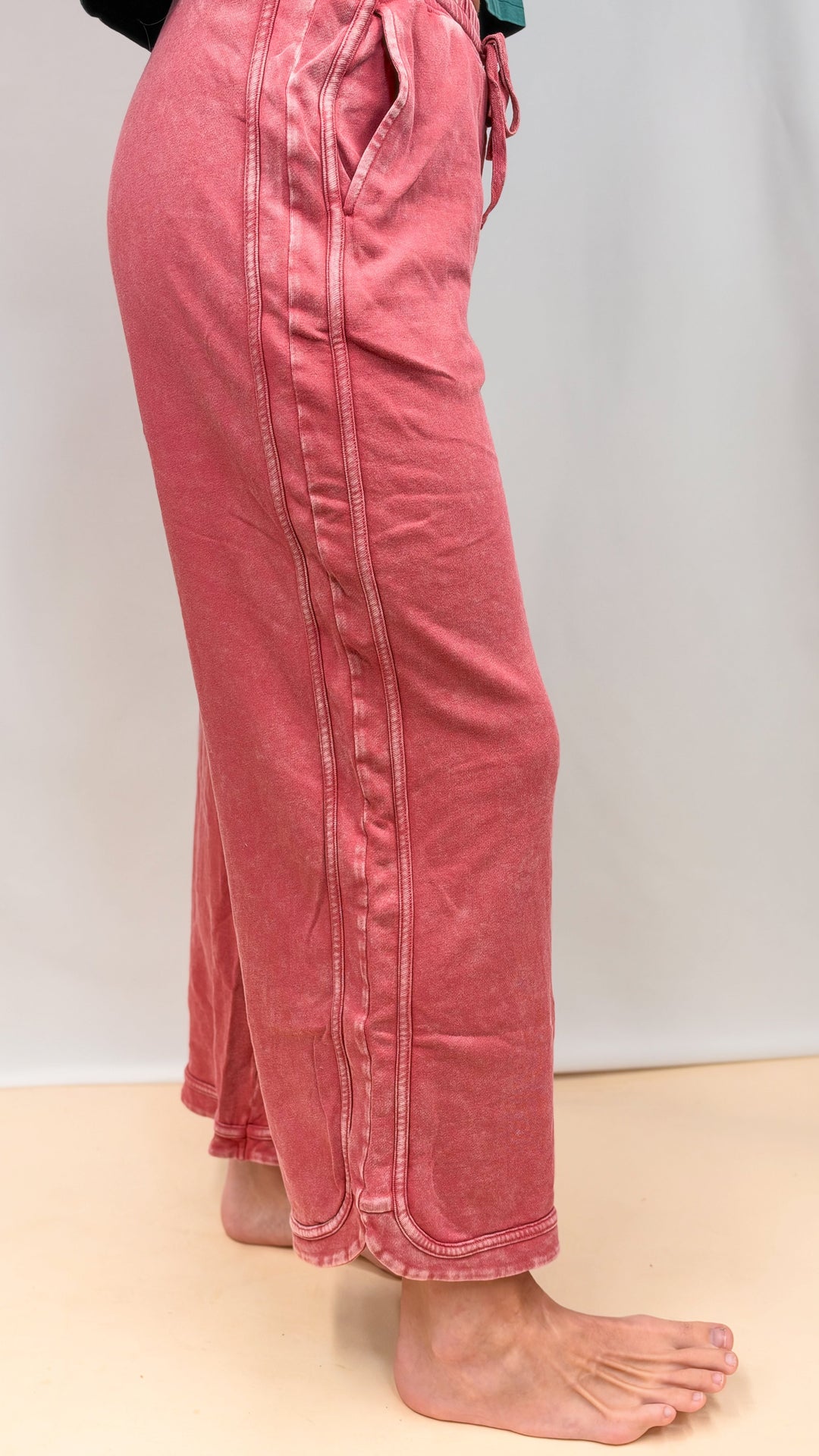 Woman shown from side view wearing raspberry color pants on plain background
