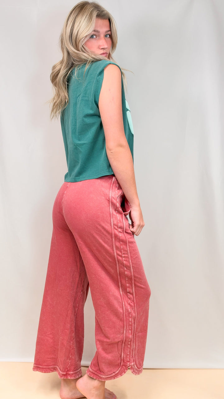 Woman wearing teal muscle tee and raspberry color pants on plain background