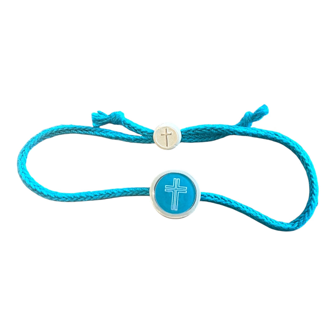 A turquoise blue cord bracelet featuring a round turquoise and silver centerpiece with a white cross, and a small silver adjustable sliding bead with a cross engraving.