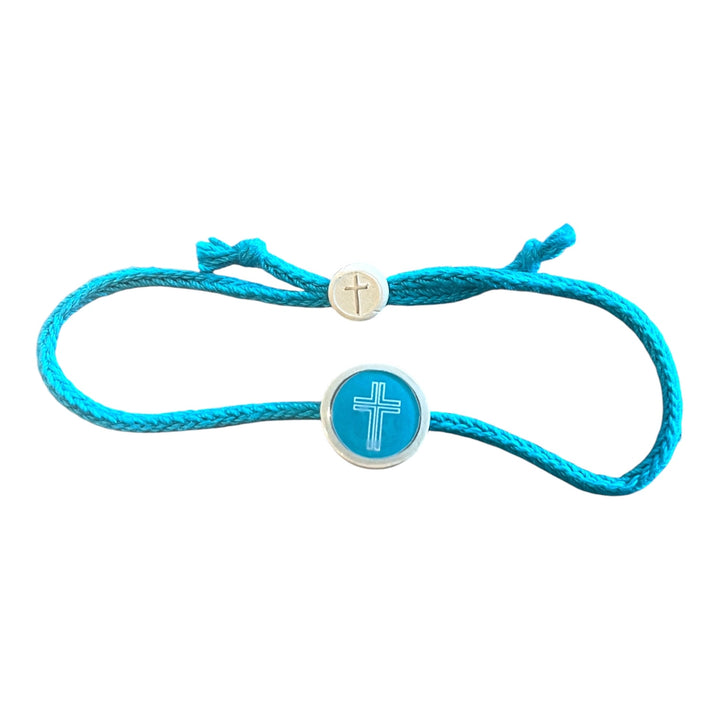 A turquoise blue cord bracelet featuring a round turquoise and silver centerpiece with a white cross, and a small silver adjustable sliding bead with a cross engraving.