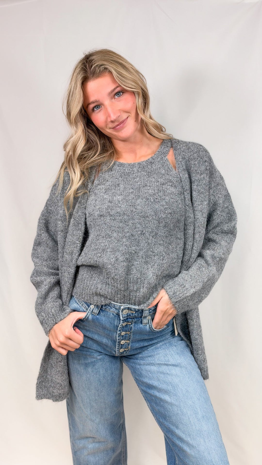 Woman wearing grey knit cardigan with matching tank top and jeans on plain background