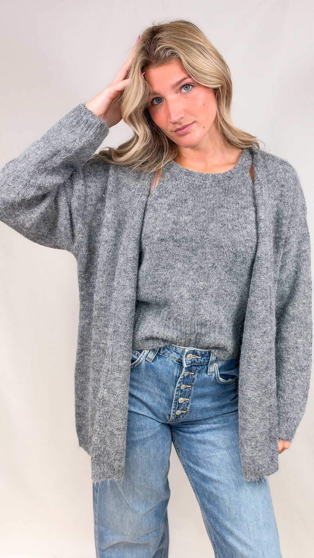 Woman wearing grey knit cardigan and matching tank with jeans on plain background