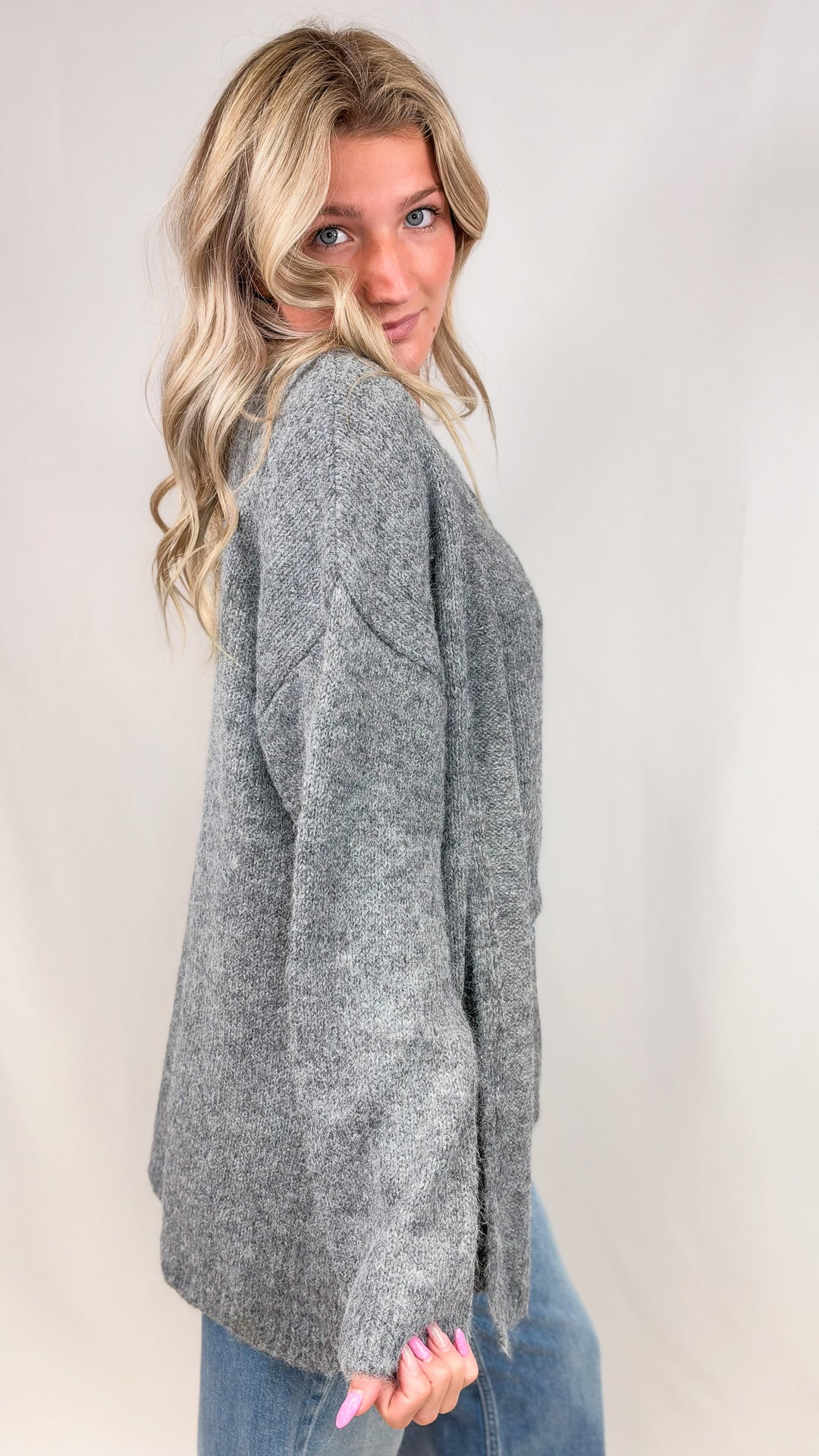 Woman wearing grey knit cardigan with jeans on plain background