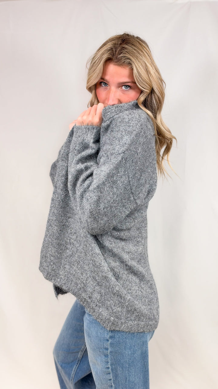 Woman wearing grey knit cardigan with jeans on plain background
