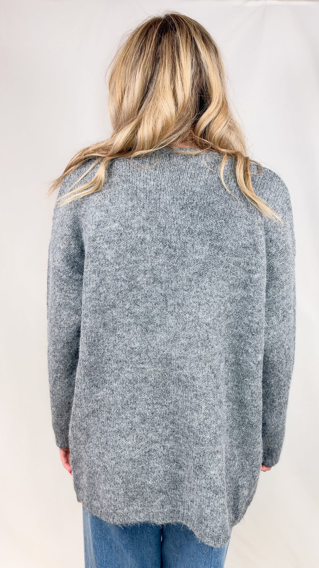 Woman shown from back wearing grey knit cardigan and jeans on plain background