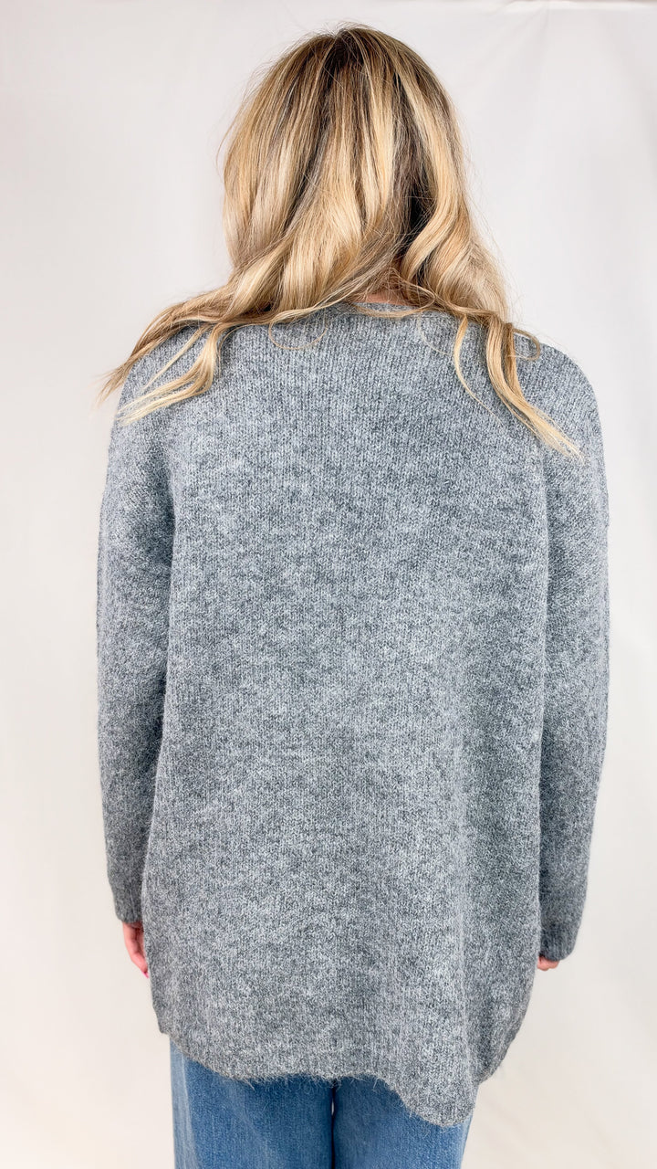 Woman shown from back wearing grey knit cardigan and jeans on plain background