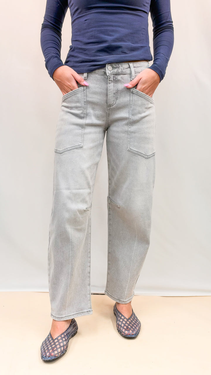 Woman wearing navy top with grey wash denim jeans and blue jelly flats on plain background