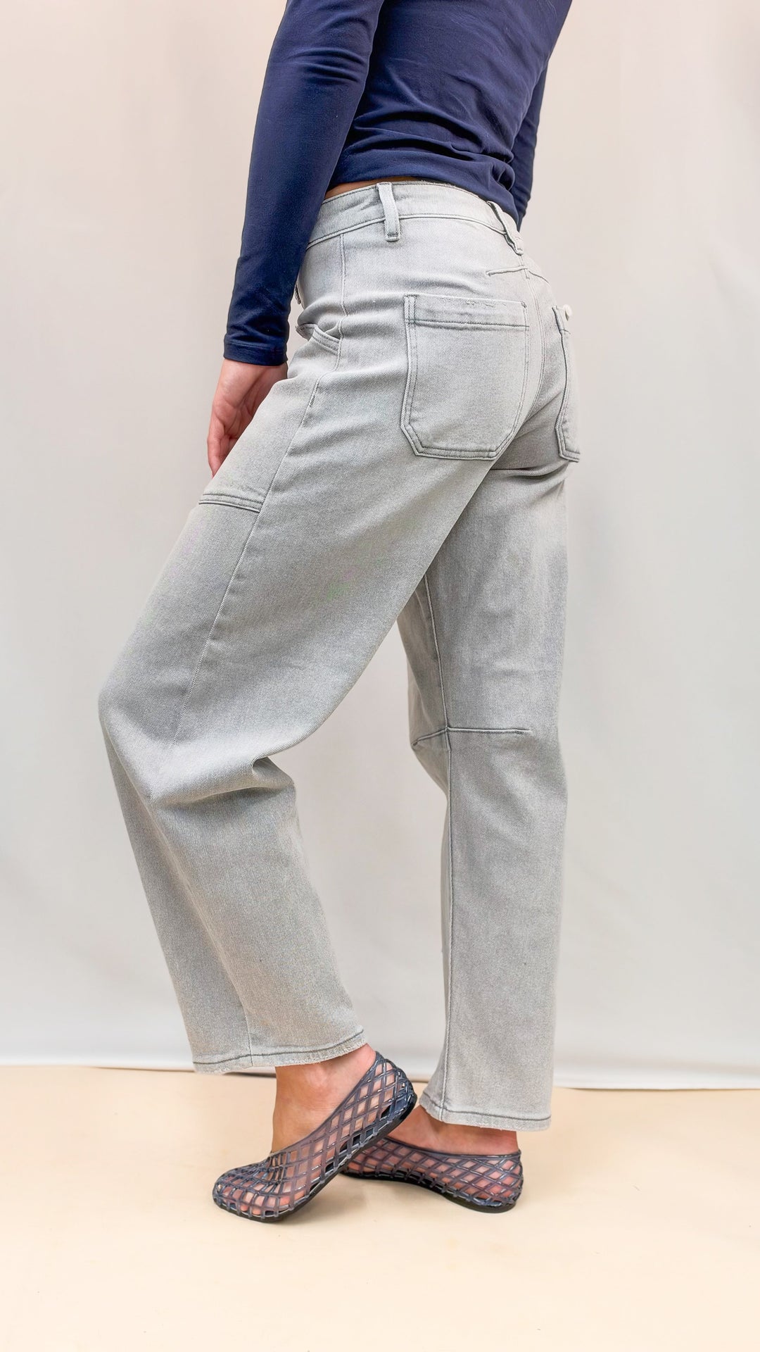 Woman wearing navy top and grey wash denim jeans with blue jelly flats on plain background
