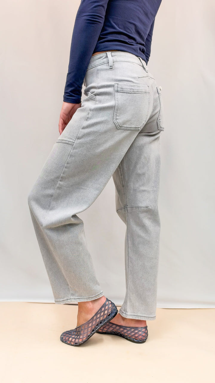 Woman wearing navy top and grey wash denim jeans with blue jelly flats on plain background