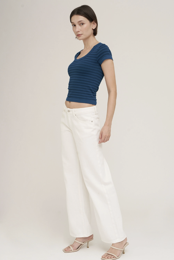 A woman modeling a navy blue short-sleeve ribbed crop top and white wide-leg pants against a plain light beige studio background.