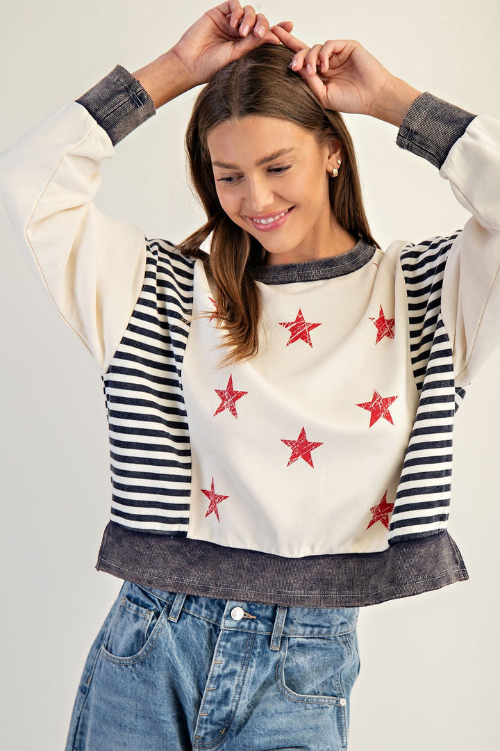 Woman wearing a sweater with star patterns and striped sleeves against a plain background