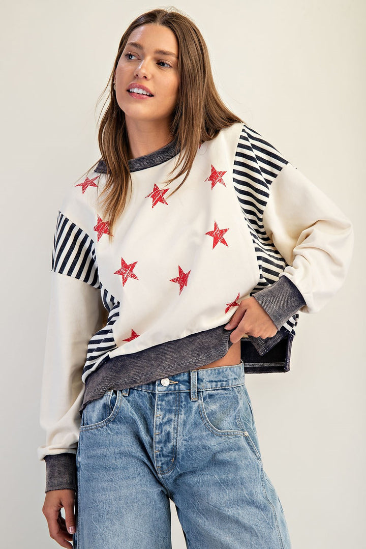 Woman wearing a white sweater with red star patterns and blue jeans on a plain background