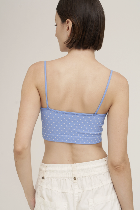 A woman shown from the back wearing a light blue spaghetti-strap crop top with a white polka dot pattern and white pants, set against a plain light beige background.