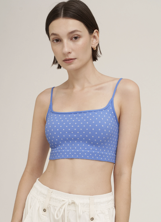 A woman wearing a blue crop top with a white polka dot pattern and white drawstring pants, photographed against a plain light beige studio background.