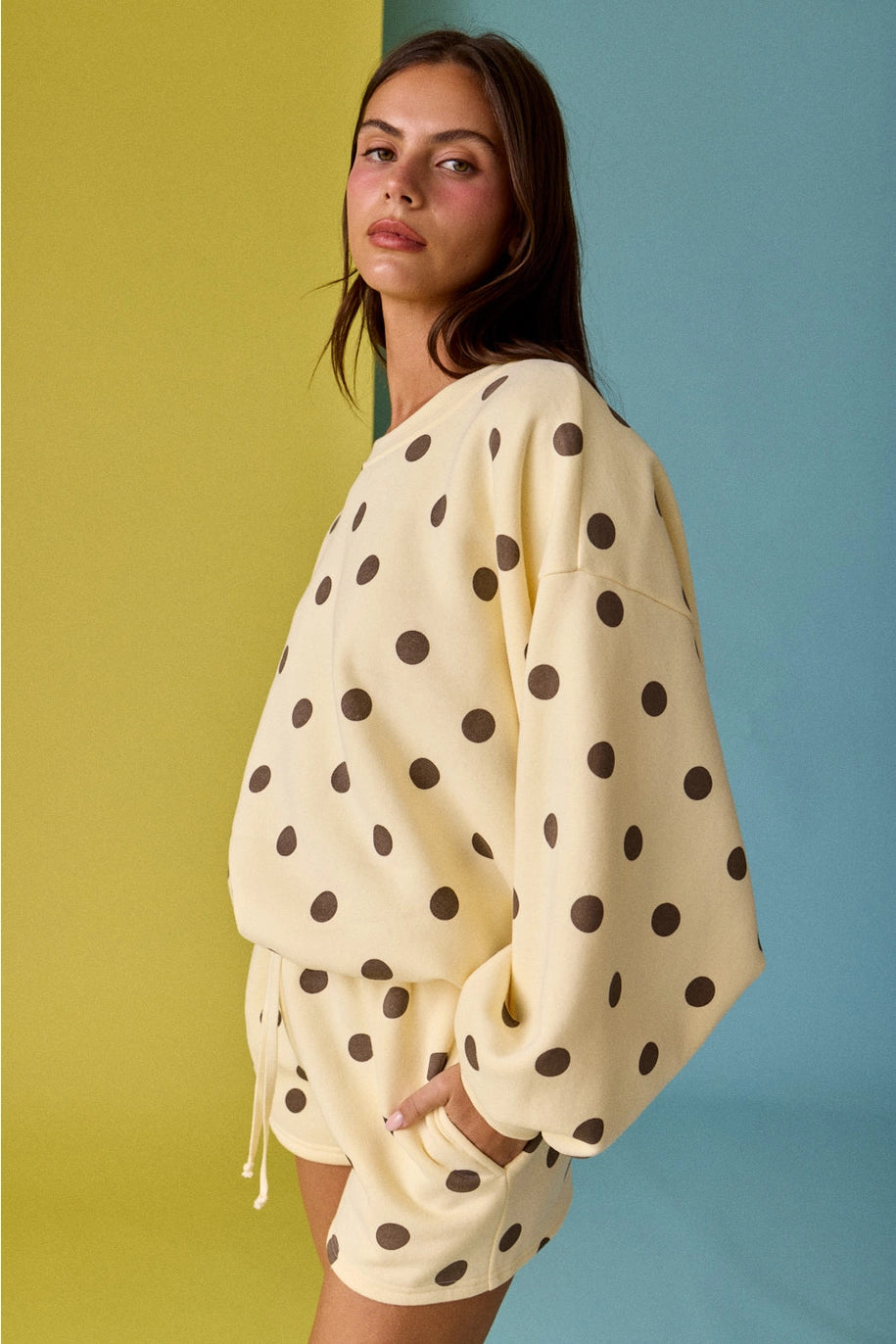 Woman wearing a cream-colored outfit with black polka dots against a multicolored background