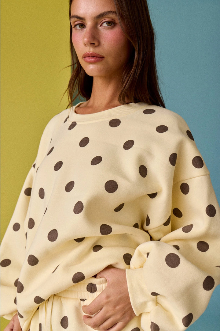 Woman wearing a cream-colored sweater with brown polka dots against a multicolored background