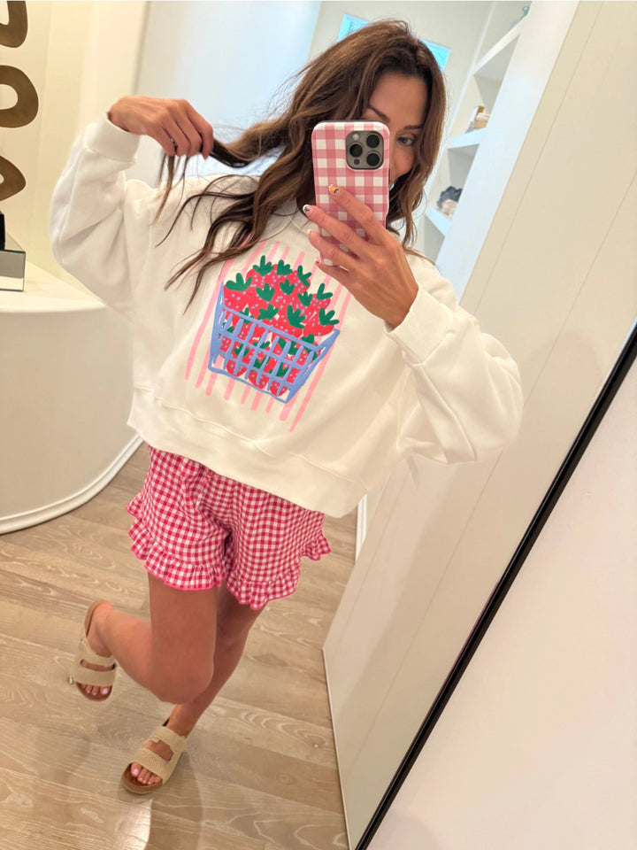 Woman wearing white sweatshirt with strawberry graphic and red plaid shorts 