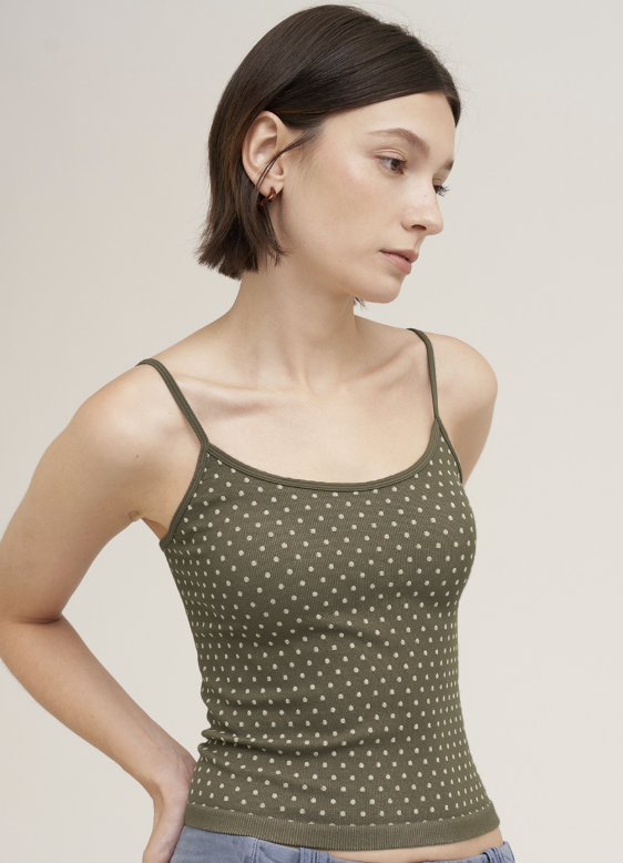 Woman wearing green tank with white polka dots on plain background