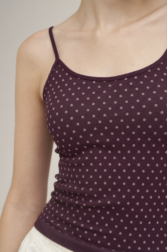 A close-up of a model wearing a dark plum purple ribbed camisole top with a small light gray polka dot pattern.