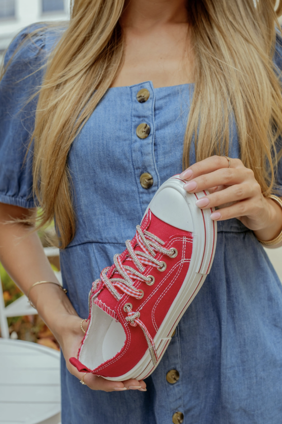 Person holding a red sneaker with white sole, wearing a blue dress.