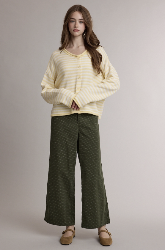 A model stands against a plain light gray studio background wearing a cream and yellow striped cardigan, olive green wide-leg pants, and tan flats.